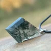 Diamond-shaped moss agate pendant resting on wood with a dark cord