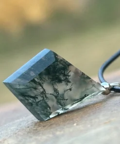 Diamond-shaped moss agate pendant resting on wood with a dark cord