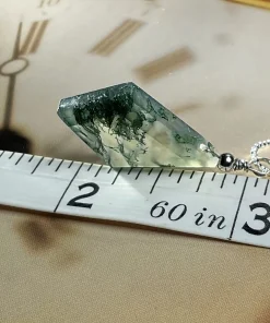 Diamond-shaped moss agate pendant beside tape measure markings
