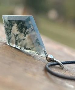 Diamond-shaped moss agate pendant standing upright on a wooden surface