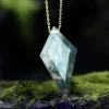 Faceted kite moss agate pendant with gold-colored chain displayed among green moss
