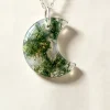 Carved crescent moon moss agate pendant with green mineral patterns on an ivory background