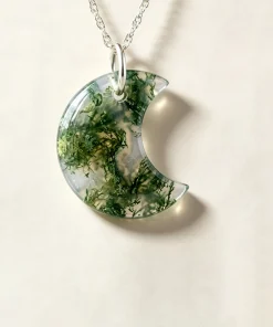 Carved crescent moon moss agate pendant with green mineral patterns on an ivory background