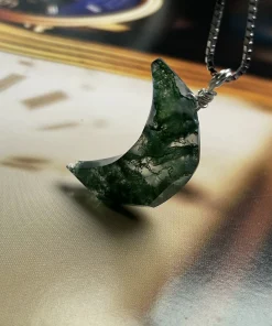 Faceted crescent moon moss agate pendant displayed on a clock-face background