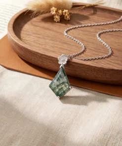 Kite moss agate pendant with silver flower motif displayed beside a wooden tray