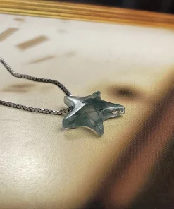 Moss agate star pendant lying on a clock-face background with its chain