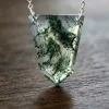 Geometric shield-shaped moss agate pendant suspended above dark wood