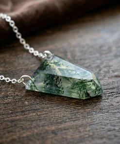 Side view of shield-shaped moss agate pendant resting on wood