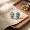 Hexagon moss agate stud earrings displayed on linen beside a wooden tray