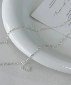 Silver-colored chain displayed on ivory fabric beside a card