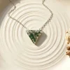 Natural triangle moss agate pendant displayed on a ridged ivory dish