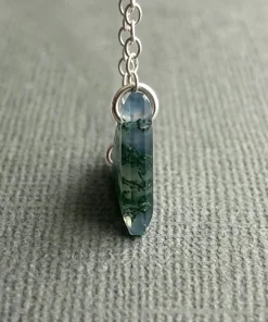 Side view of triangular moss agate pendant on gray fabric