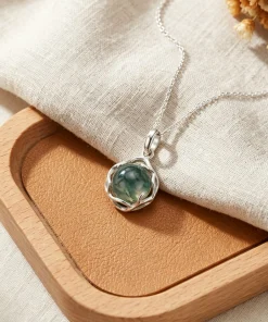 Organic vine-frame moss agate necklace displayed on linen beside a wooden tray