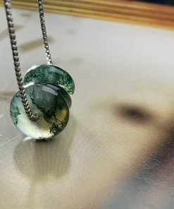 Angled view of three round moss agate discs on a box chain