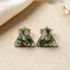 Triangle moss agate stud earrings with gold-colored central details on ivory fabric