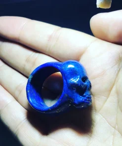 Hand-carved lapis lazuli skull ring resting on a hand