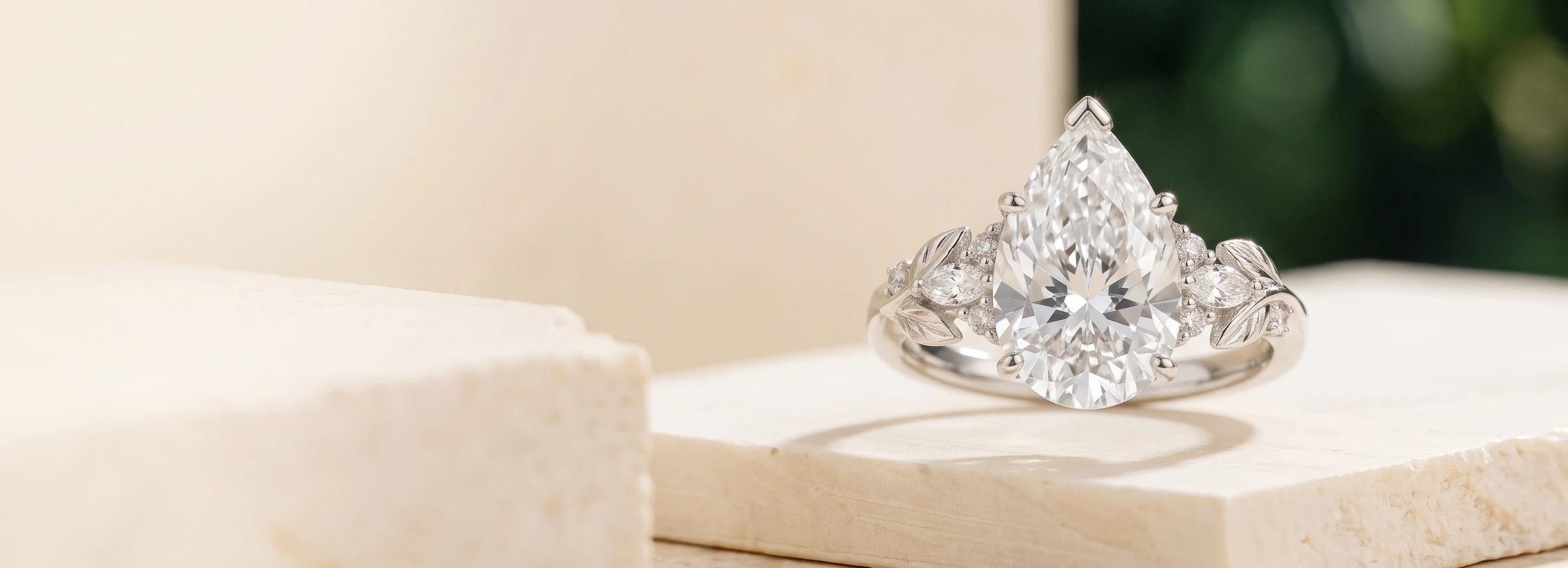 Illustrative pear-shaped diamond ring in white metal with leaf details and accent stones