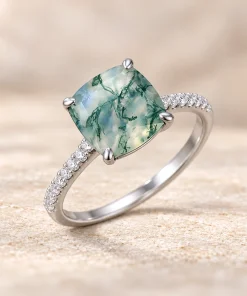 Angled view of cushion-cut moss agate ring with a white gold band and clear accents